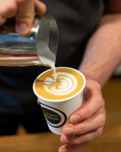 A Two Beans employee perfectly crafting a beautiful latte.