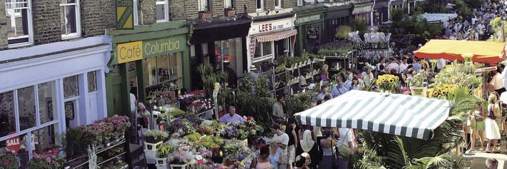 An aerial image of Columbia Road Flower Market on a busy Sunday with a street full of stalls selling flowers with cafes that overlook the market