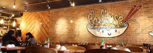 Inside Pho House, one restaurant along Pho Mile in Shoreditch with a mural of a cartoon bowl of Pho on a red brick wall